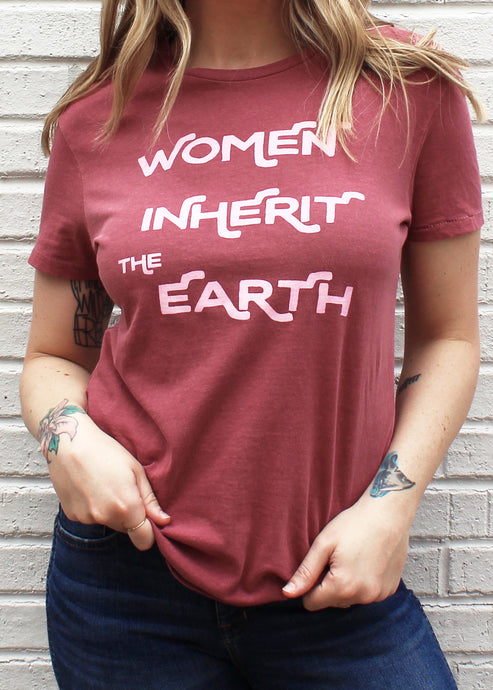 Female modeling red unisex graphic tee with pink print that reads Women Inherit the Earth.